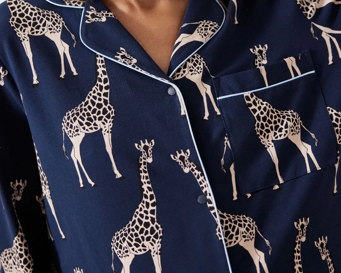 A close-up of a person wearing navy blue pajama top with a beige giraffe print and white piping trim.