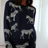 A woman wearing a navy blue long-sleeve top with an all-over white zebra print, shown from the waist up against a bright white curtain background.