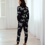 A woman wearing a matching two-piece pajama set with a zebra print, standing barefoot in a bright room with white curtains and light wood floors.