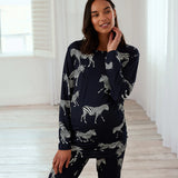 A woman modeling a matching two-piece pajama set featuring a dark navy blue base with a white zebra print, posed in a bright, minimalist room with white walls and light wood flooring.