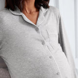 A close-up of a pregnant model wearing a light gray heather long-sleeve maternity button-up shirt with white piping and a chest pocket.