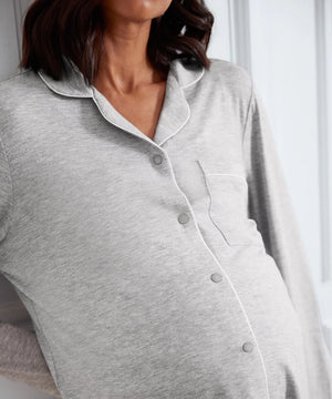 A close-up of a pregnant model wearing a light gray heather long-sleeve maternity button-up shirt with white piping and a chest pocket.