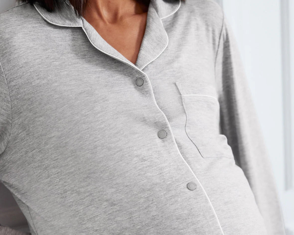 A close-up of a pregnant model wearing a light gray heather long-sleeve maternity button-up shirt with white piping and a chest pocket.