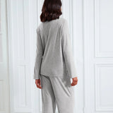 A woman viewed from behind wearing a light gray two-piece loungewear set, consisting of a long-sleeve top and matching pants, standing in front of white paneled doors.
