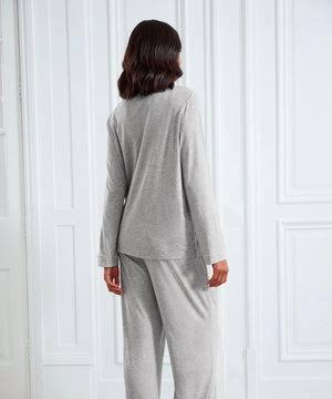 A woman viewed from behind wearing a light gray two-piece loungewear set, consisting of a long-sleeve top and matching pants, standing in front of white paneled doors.