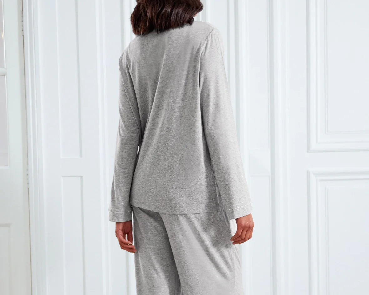 A woman viewed from behind wearing a light gray two-piece loungewear set, consisting of a long-sleeve top and matching pants, standing in front of white paneled doors.