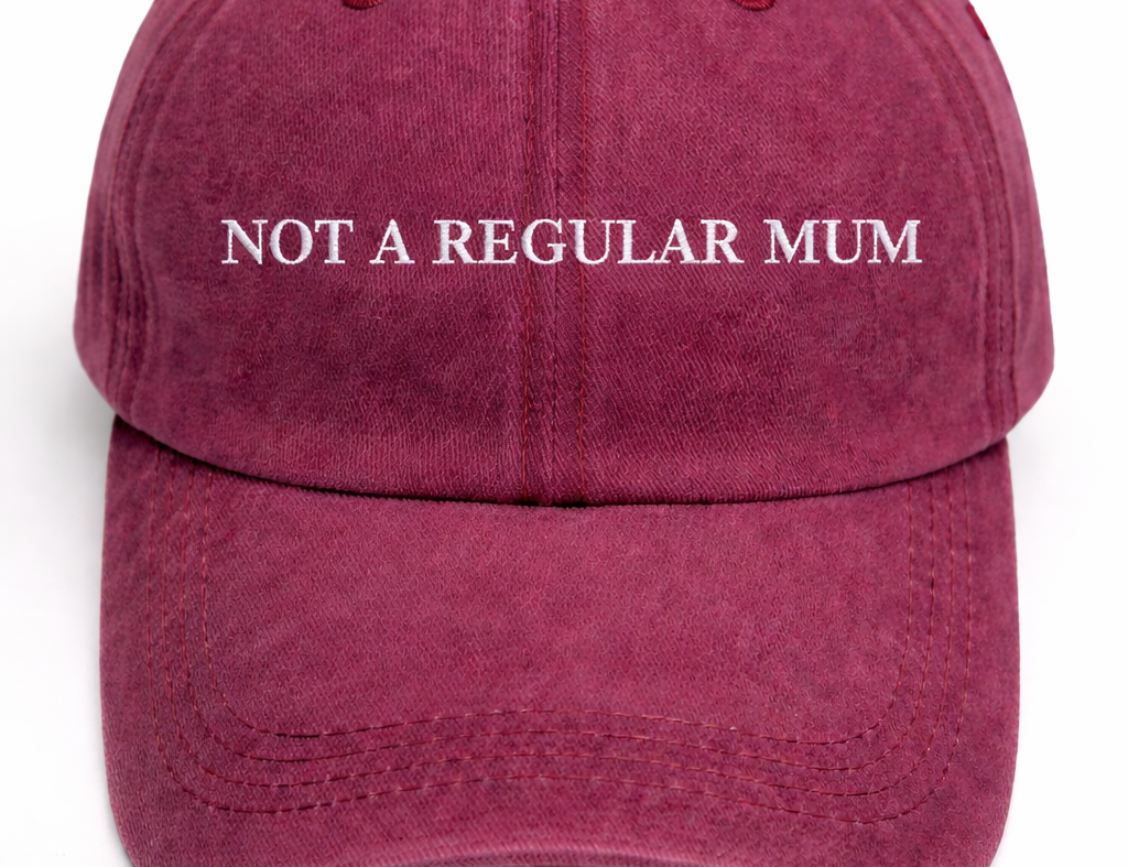 A washed burgundy baseball cap with the phrase 'NOT A REGULAR MUM' embroidered in white across the front, shown against a plain white background.