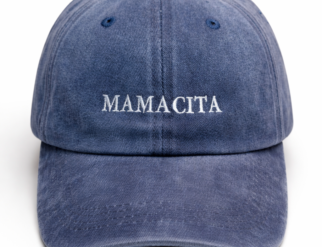 A washed blue denim baseball cap with 'MAMACITA' embroidered in white across the front, shown against a plain white background.