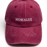 A dusty burgundy baseball cap with 'MOMAGER' embroidered in white on the front, shown against a plain white background.