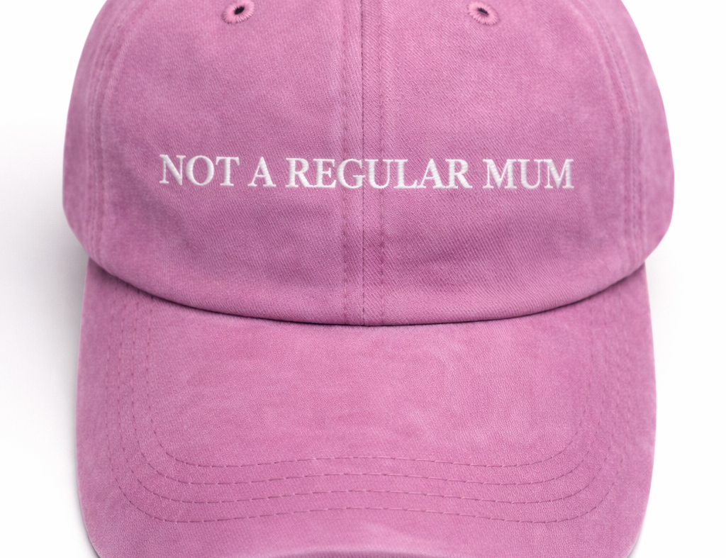 A pink distressed baseball cap with the phrase 'NOT A REGULAR MUM' embroidered in white across the front, shown against a plain white background.