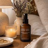 Sleepy Head Pillow Spray on a bedside table with dried lavender and chamomile in a vase, a lit candle and a lamp