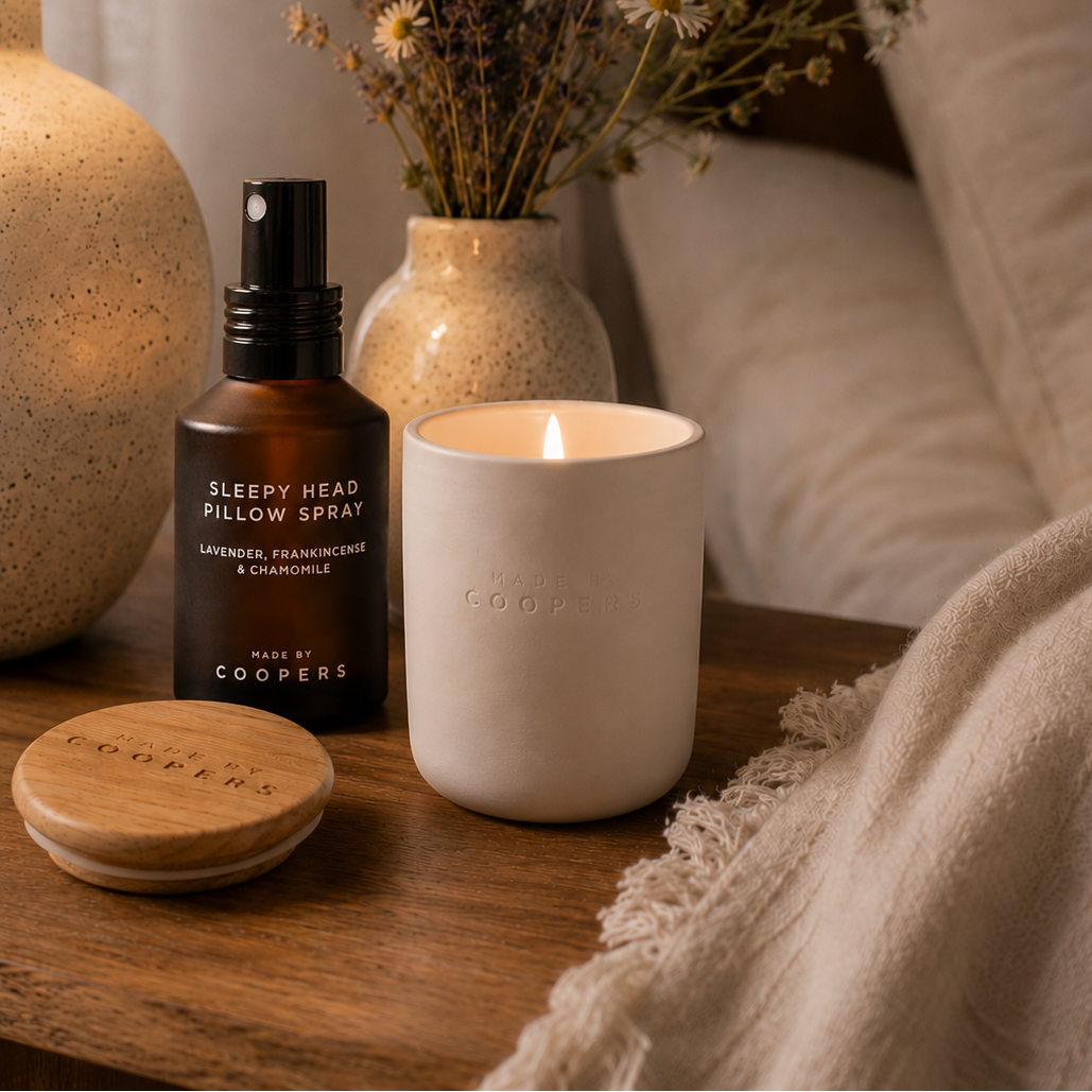 Sleepy Head Pillow Spray beside a lit Made by Coopers candle and its wooden lid on a bedside table