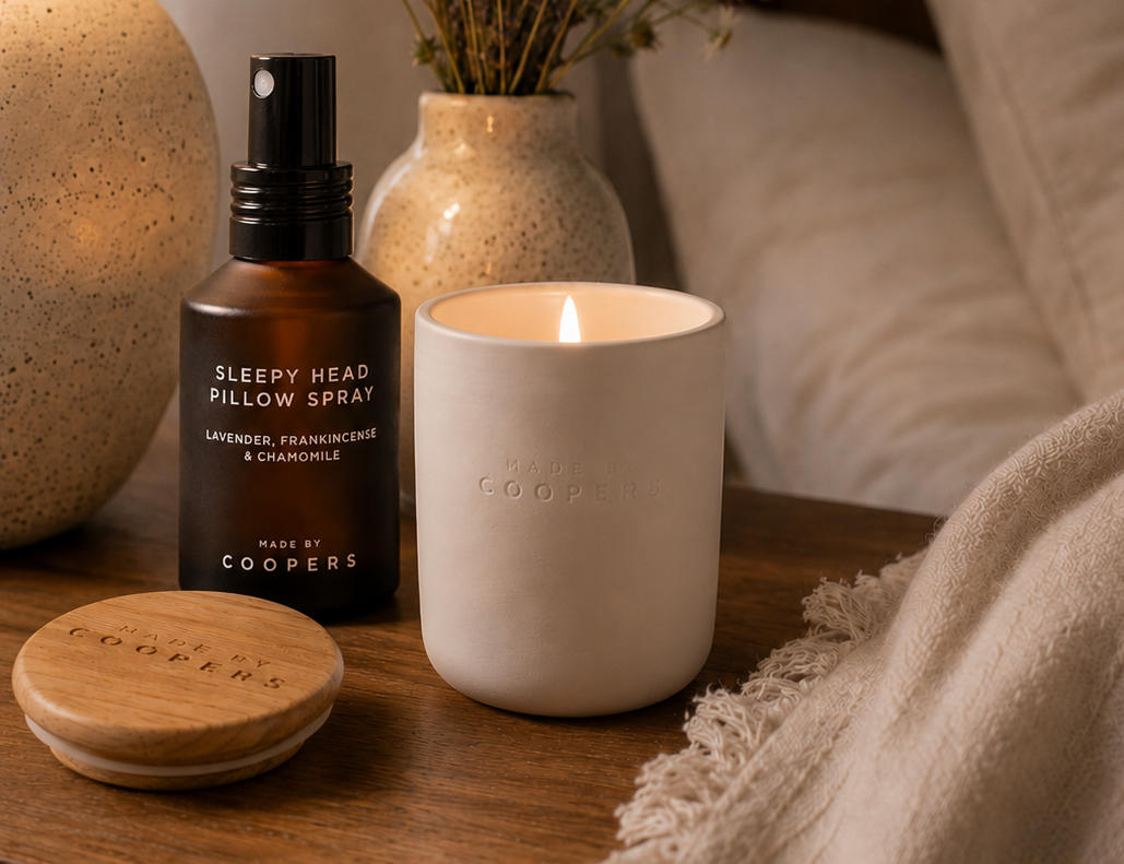Sleepy Head Pillow Spray beside a lit Made by Coopers candle and its wooden lid on a bedside table