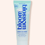 A squeeze tube of bloom balm Cheek to Cheek baby balm, featuring a light blue and white design with dark blue text, set against a solid pale peach background.