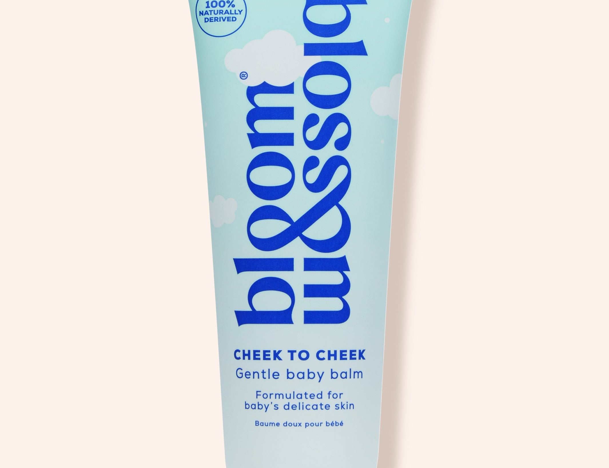 A squeeze tube of bloom balm Cheek to Cheek baby balm, featuring a light blue and white design with dark blue text, set against a solid pale peach background.