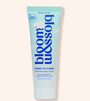 A squeeze tube of bloom balm Cheek to Cheek baby balm, featuring a light blue and white design with dark blue text, set against a solid pale peach background.