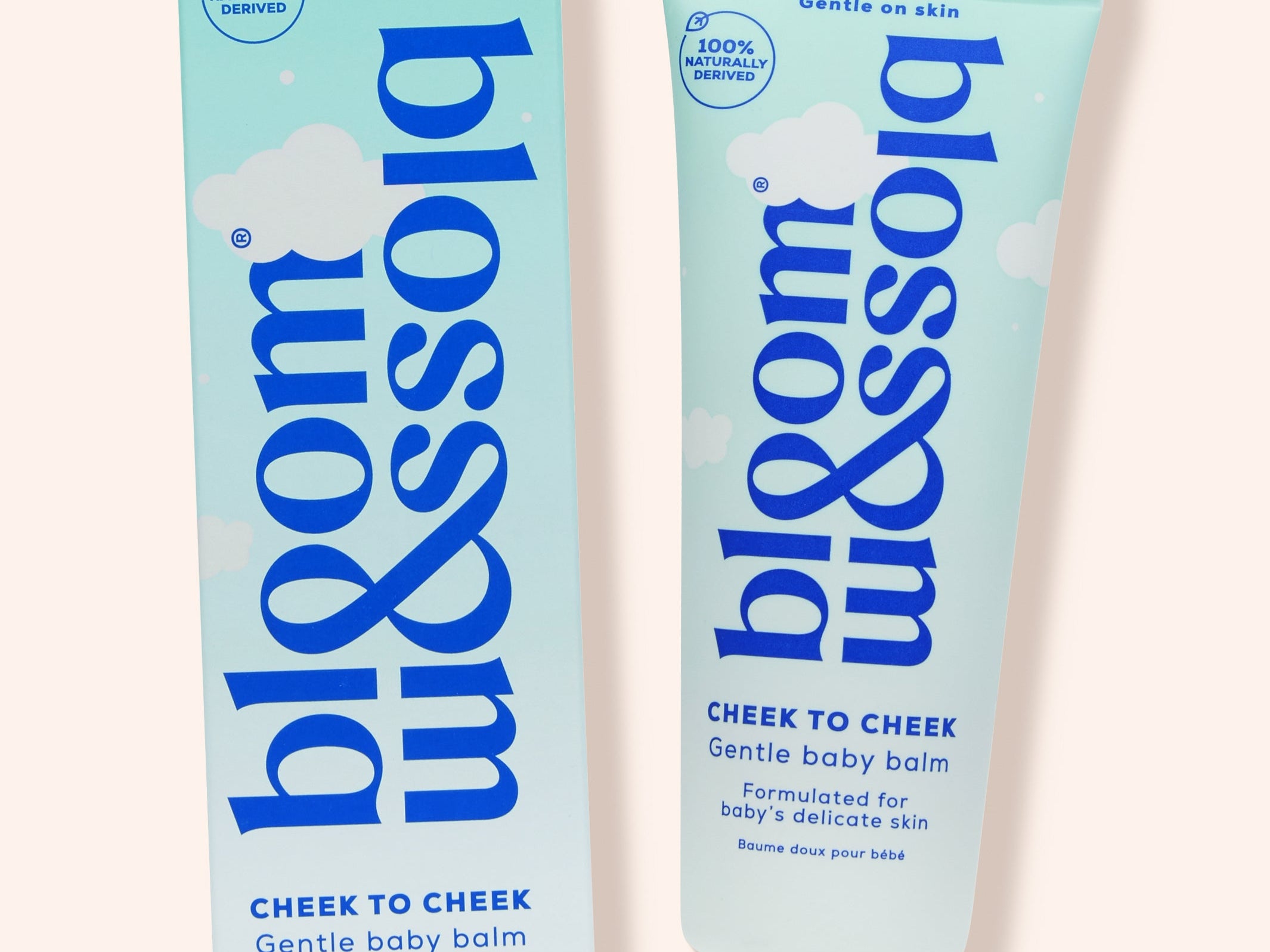 Blossom Cheek to Cheek gentle baby balm shown as a light blue squeeze tube next to its matching retail box on a pale peach background.