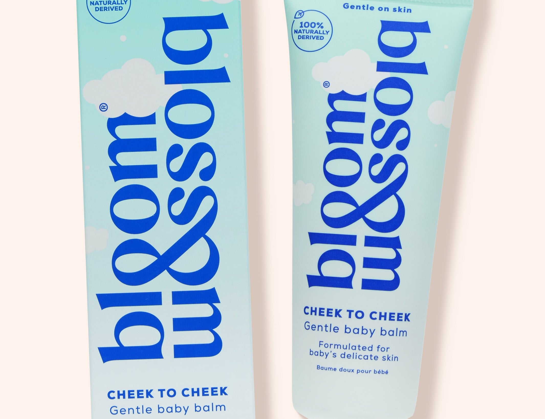 Blossom Cheek to Cheek gentle baby balm shown as a light blue squeeze tube next to its matching retail box on a pale peach background.