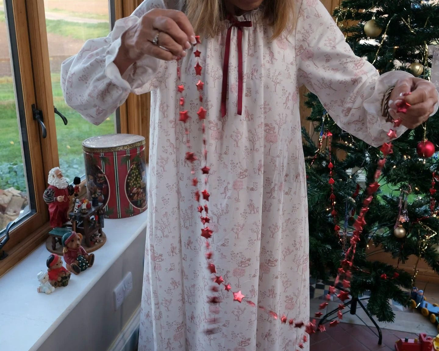Cordelia Toile nightie, full-length view on a woman holding a red star garland beside a Christmas tree