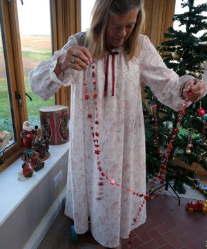 Cordelia Toile nightie, full-length view on a woman holding a red star garland beside a Christmas tree