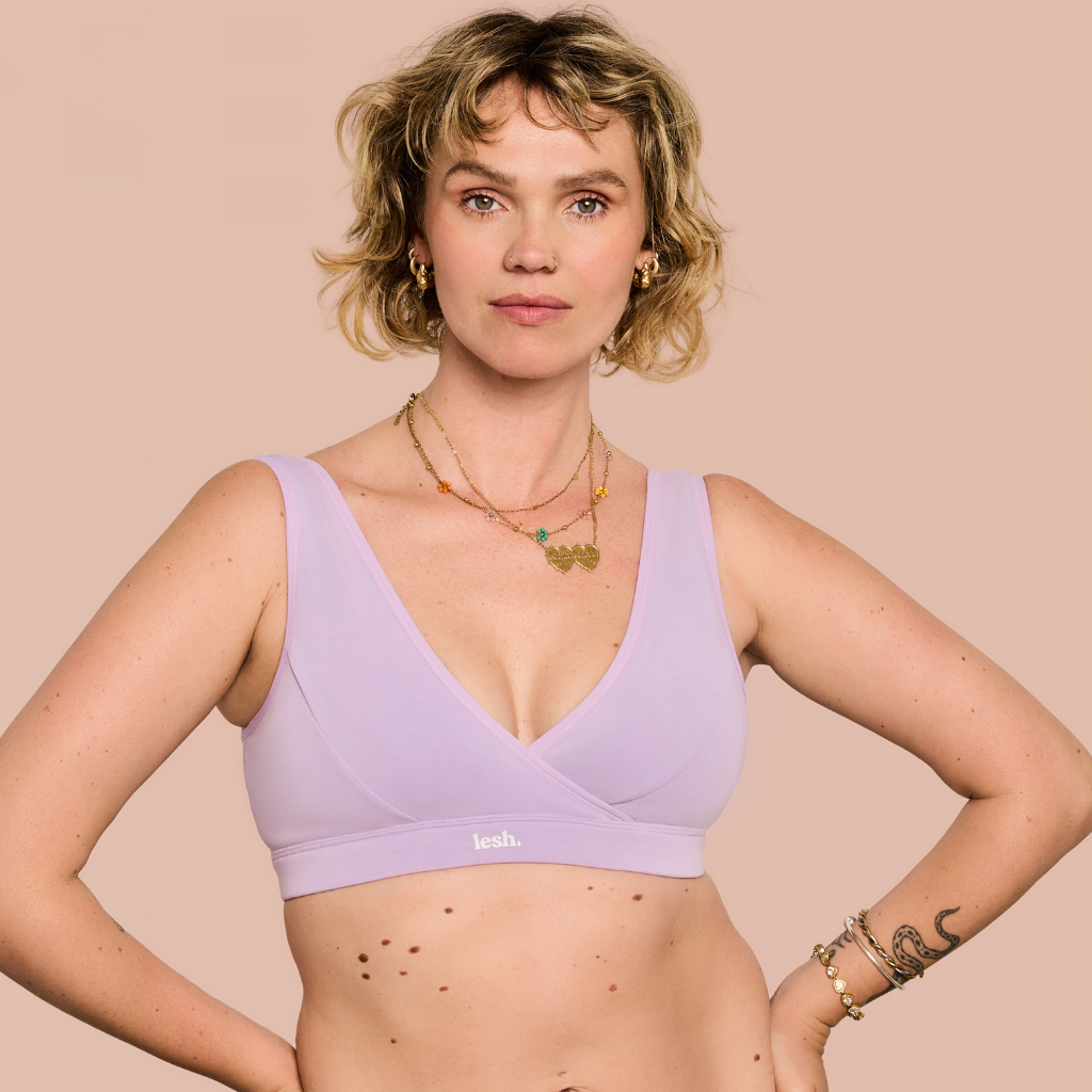 A woman modeling a light purple/lavender wrap-front bralette against a solid pale peach background. The brand name 'lulu.