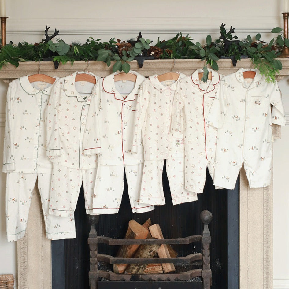 Set of pajama sets hanging on a fireplace mantle with decorative greenery.
