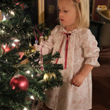 Girls' Nightie in Cordelia Toile, child in the pink toile print with red ribbon tie looking at baubles on a Christmas tree