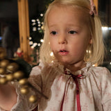Girls' Nightie in Cordelia Toile, close-up of the gathered neckline and red ribbon bow on a child holding gold baubles