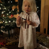 Girls' Nightie in Cordelia Toile, full-length view on a child holding a small ornament beside a lit Christmas tree