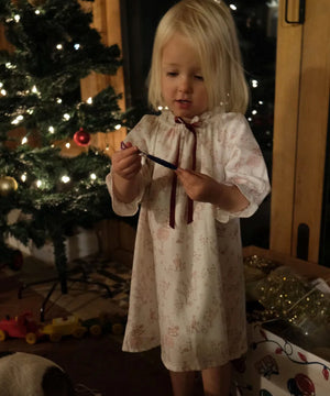 Girls' Nightie in Cordelia Toile, full-length view on a child holding a small ornament beside a lit Christmas tree