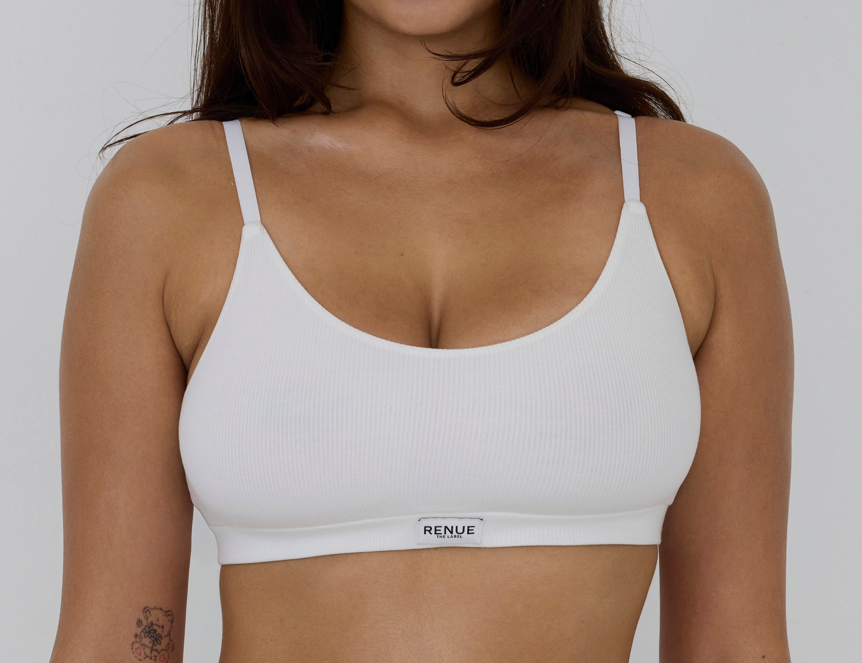 Woman wearing a white bra with 'Renue' label against a plain background
