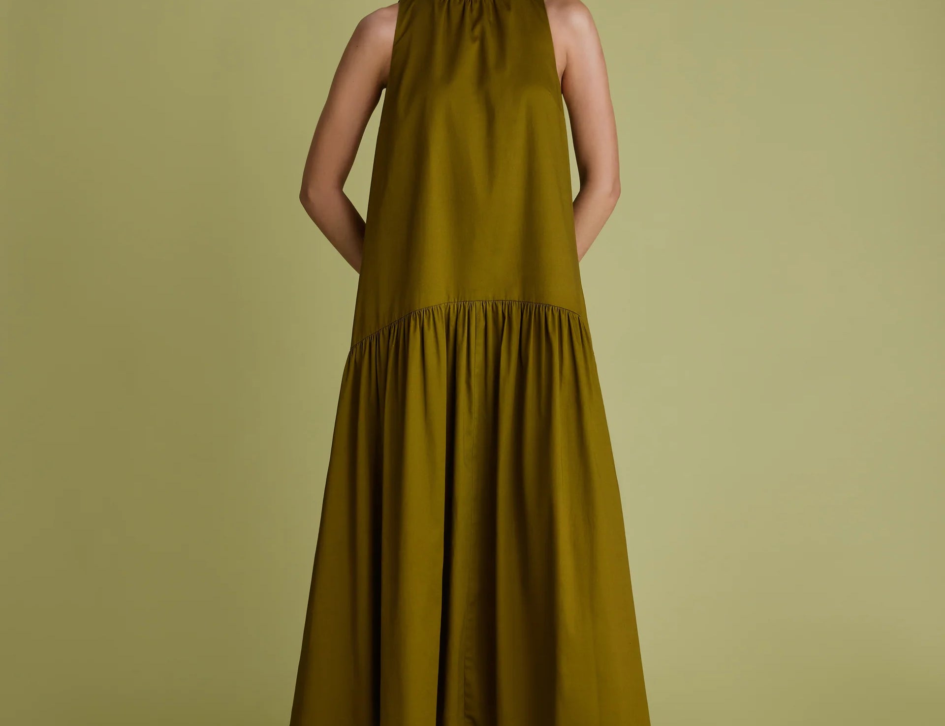 Woman wearing khaki green dress with high neck, sleeveless and a line shape