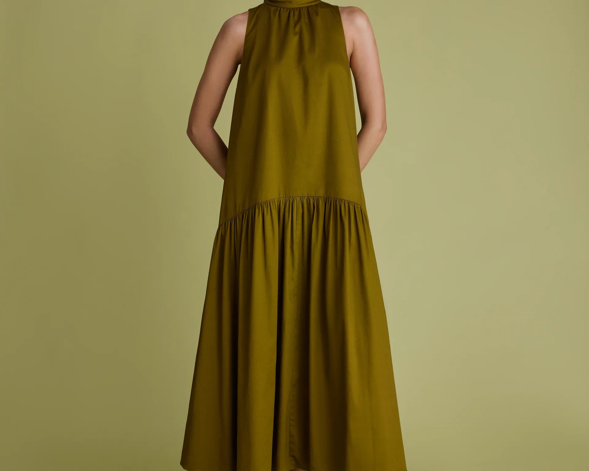 Woman wearing khaki green dress with high neck, sleeveless and a line shape