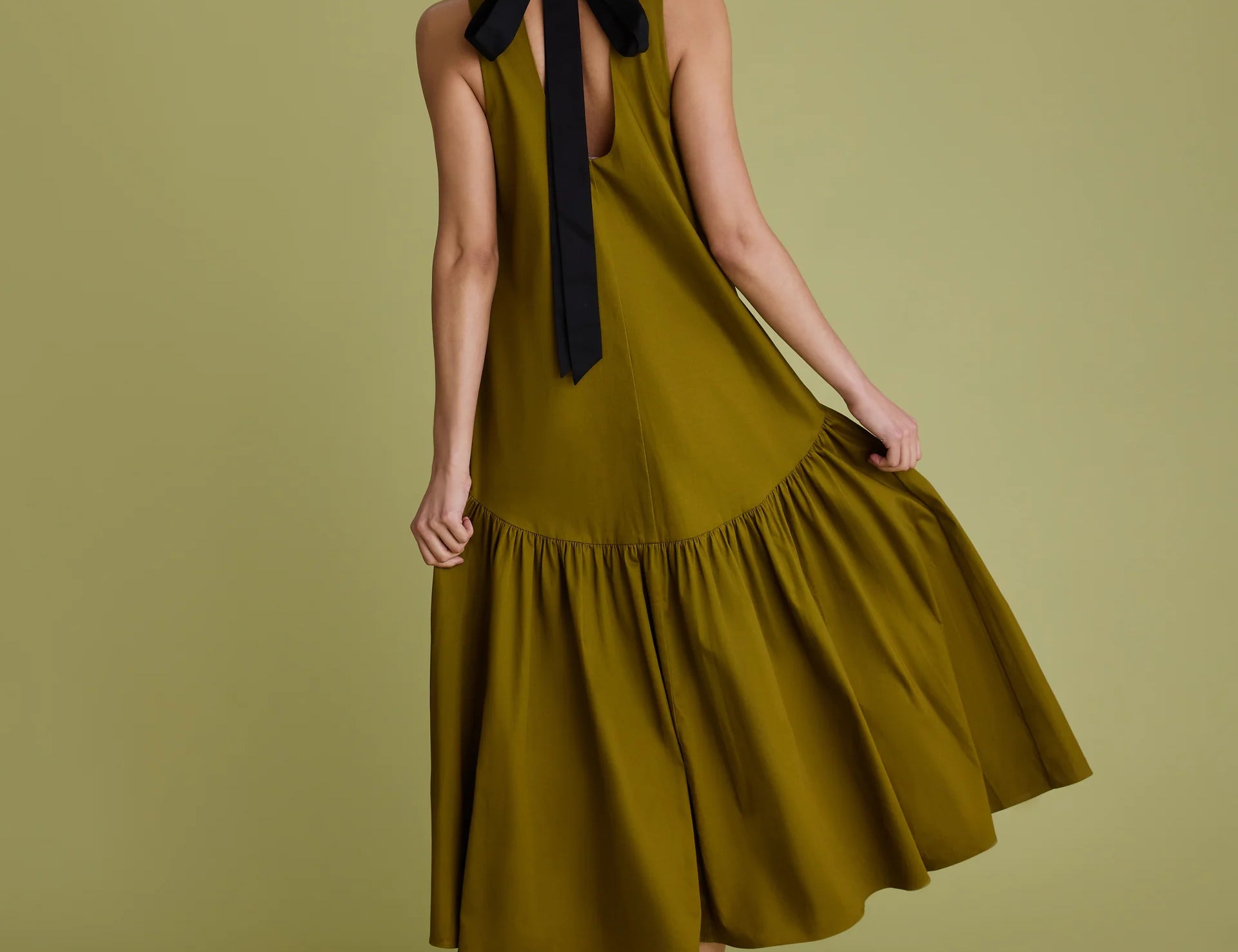 Woman wearing khaki dress with black bow at the back of the neck