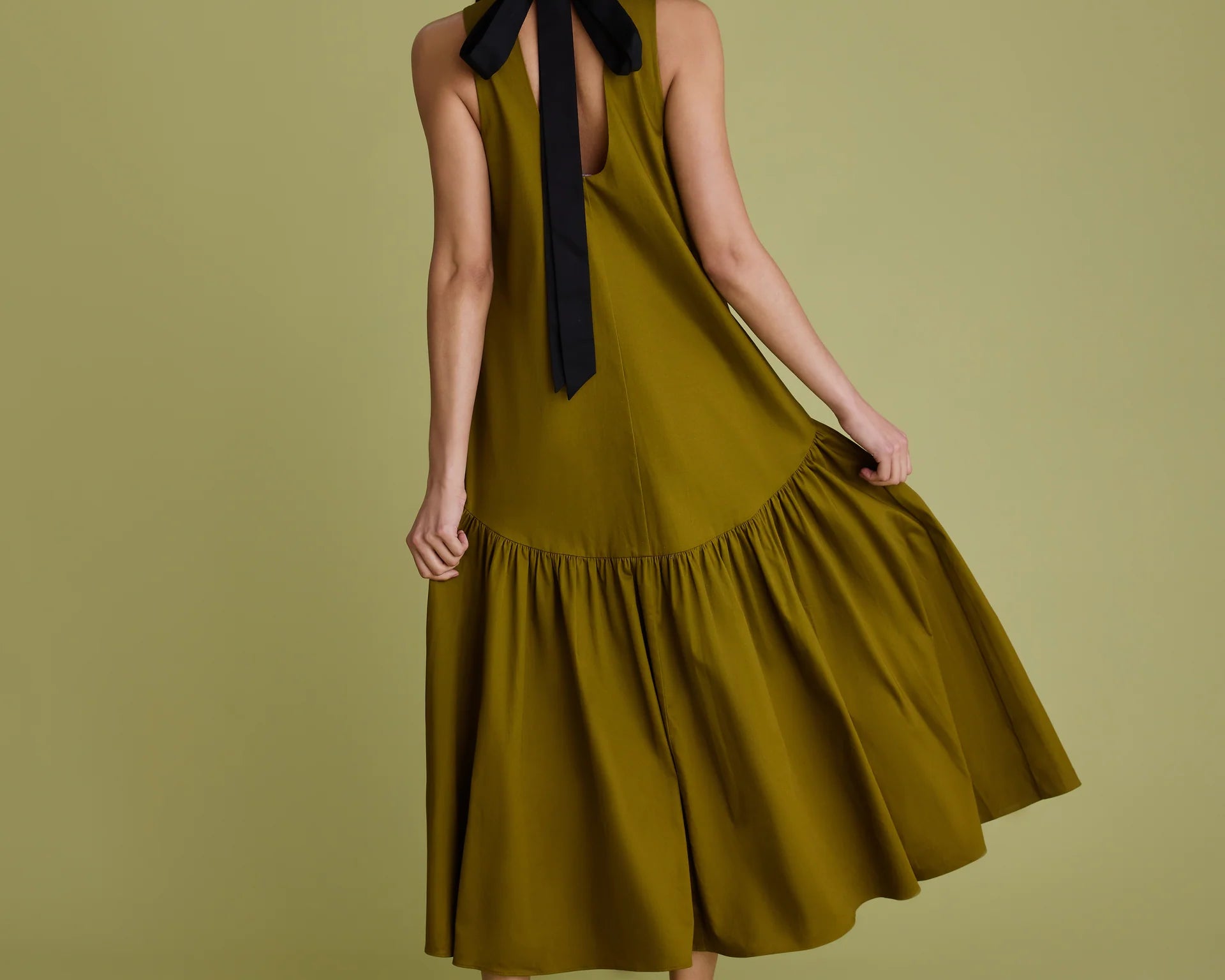 Woman wearing khaki dress with black bow at the back of the neck