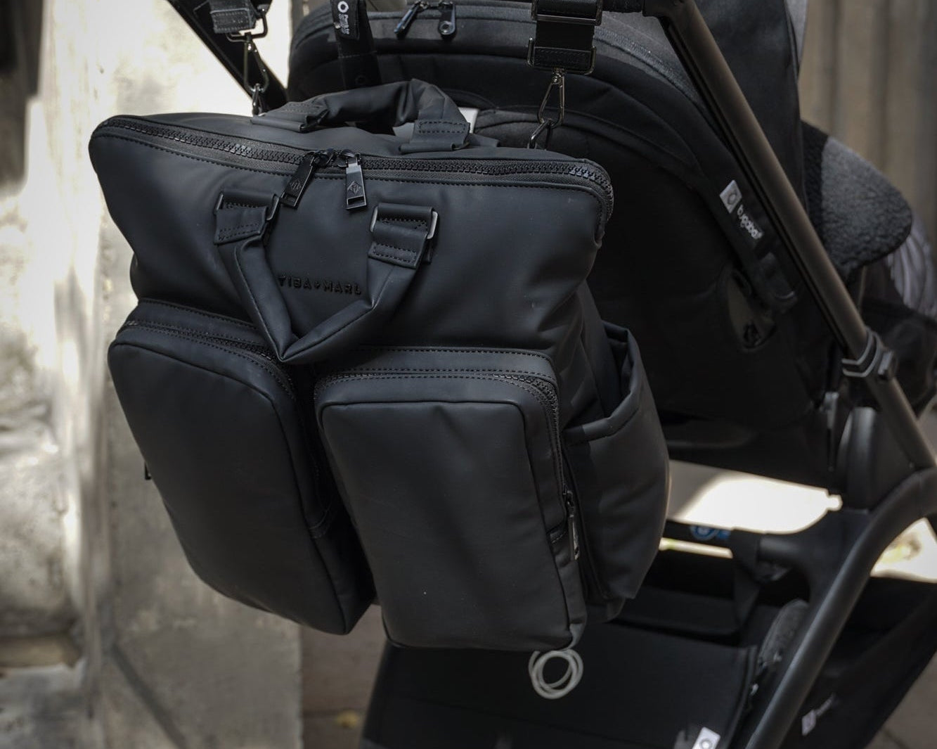 Black stroller with attached bag against a neutral background