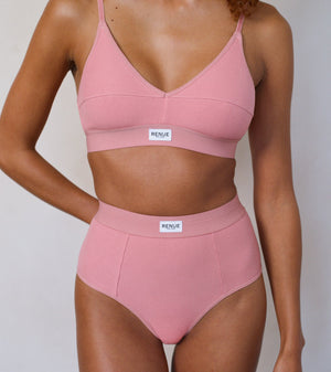 A model wearing a two-piece ribbed pink lingerie set consisting of a V-neck bralette and matching high-waisted briefs, both featuring a white rectangular 'RENUE' brand label on the waistband.