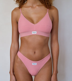 A model wearing a dusty pink two-piece bikini set with thin straps and a small white brand label on the front of each piece, set against a plain light gray background.