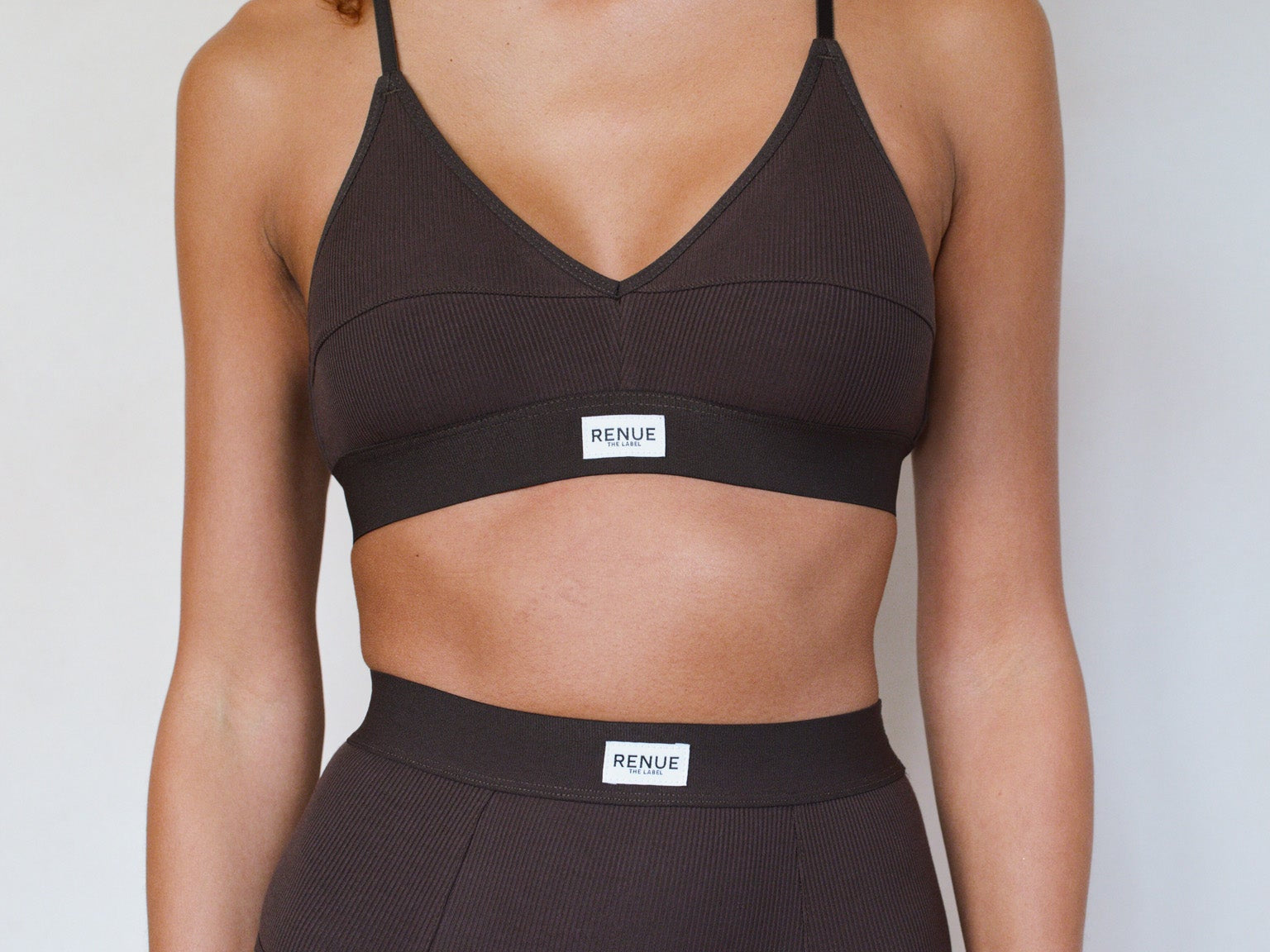 A model wearing a dark brown two-piece bikini set with a scoop neck top and high-waisted bottoms, featuring a small white brand label that reads 'HENDT'.