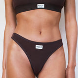 A model wearing a ribbed two-piece bikini set in dark brown, featuring a matching sports bra top and high-cut bikini bottoms with a small white brand label reading 'RENUE'.