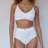 A model wearing a white two-piece lingerie set consisting of a bralette and high-waisted briefs, shown against a plain light background.
