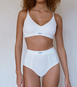 A model wearing a white two-piece lingerie set consisting of a bralette and high-waisted briefs, shown against a plain light background.