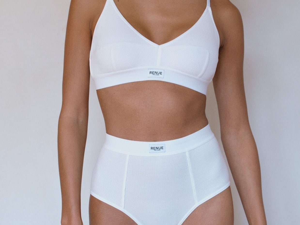 A model wearing a white two-piece lingerie set consisting of a bralette and high-waisted briefs, shown against a plain light background.