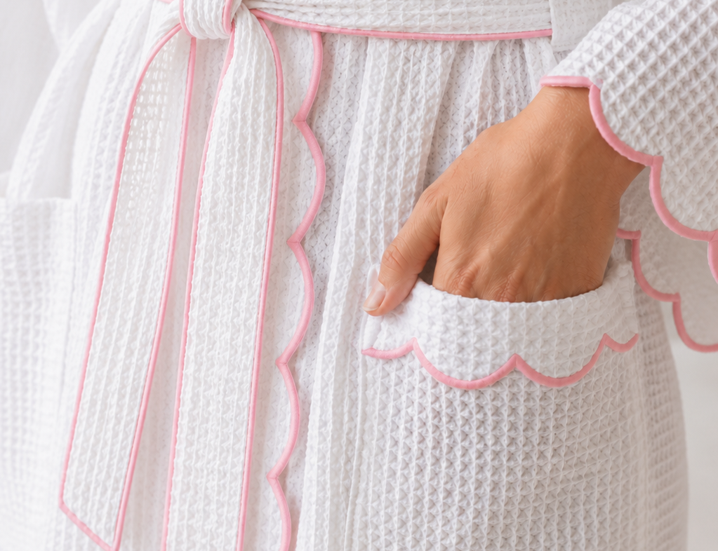 White textured robe with pink trim and a hand in the pocket against a light background