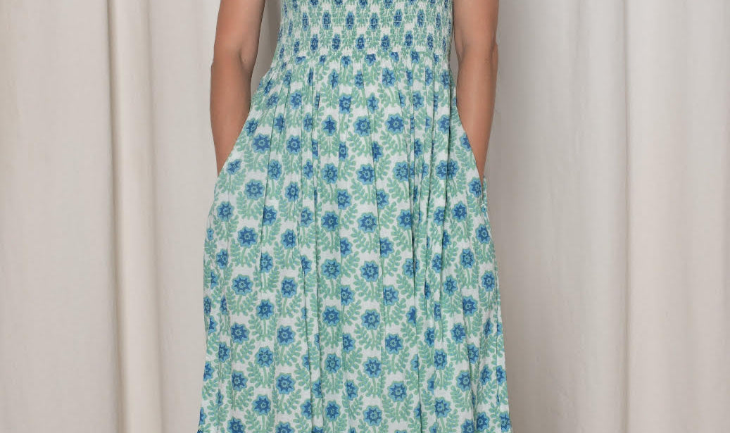Woman wearing a floral dress standing against a white curtain.