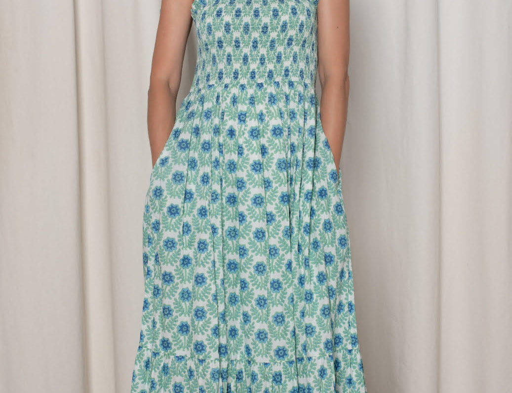 Woman wearing a floral dress standing against a white curtain.