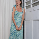 Woman wearing a floral dress standing against a white wall.