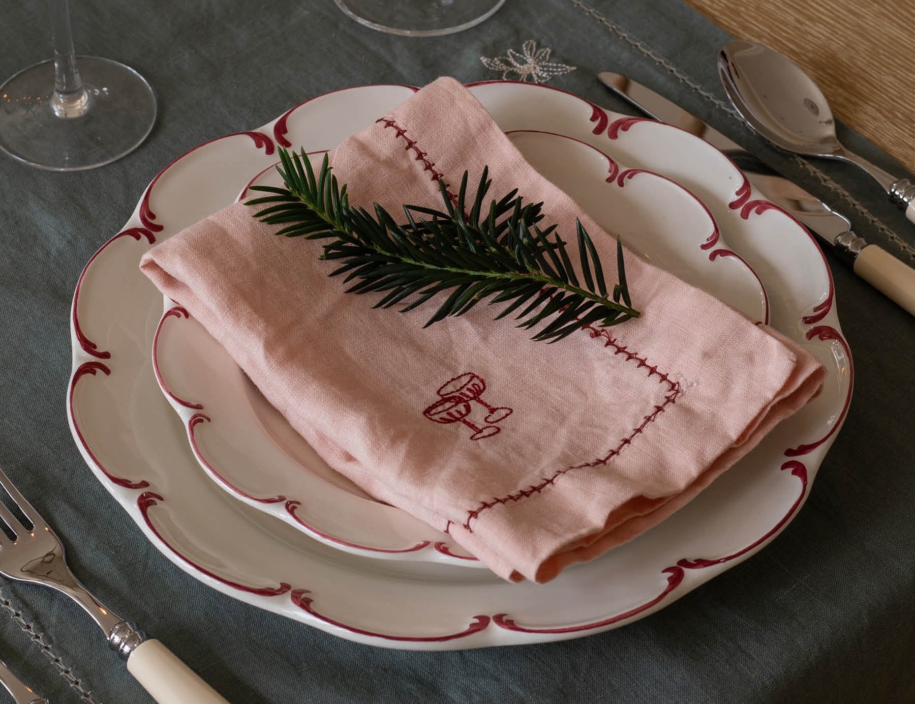 Table setting with a pink embroidered napkin on a white plate with red trim.
