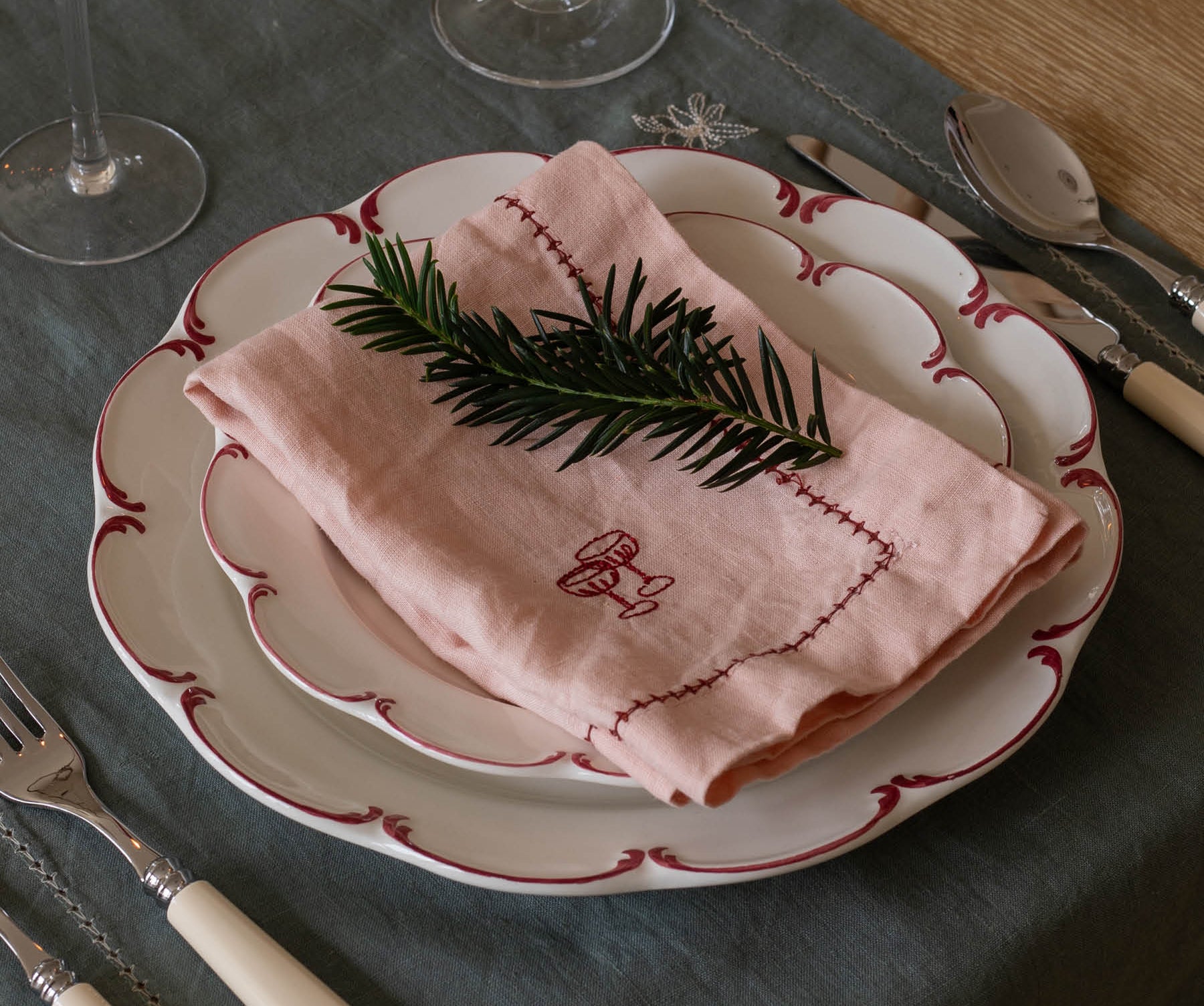 Table setting with a pink embroidered napkin on a white plate with red trim.