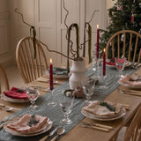 Dining table set for a meal with Christmas decorations, including a tree and candles.